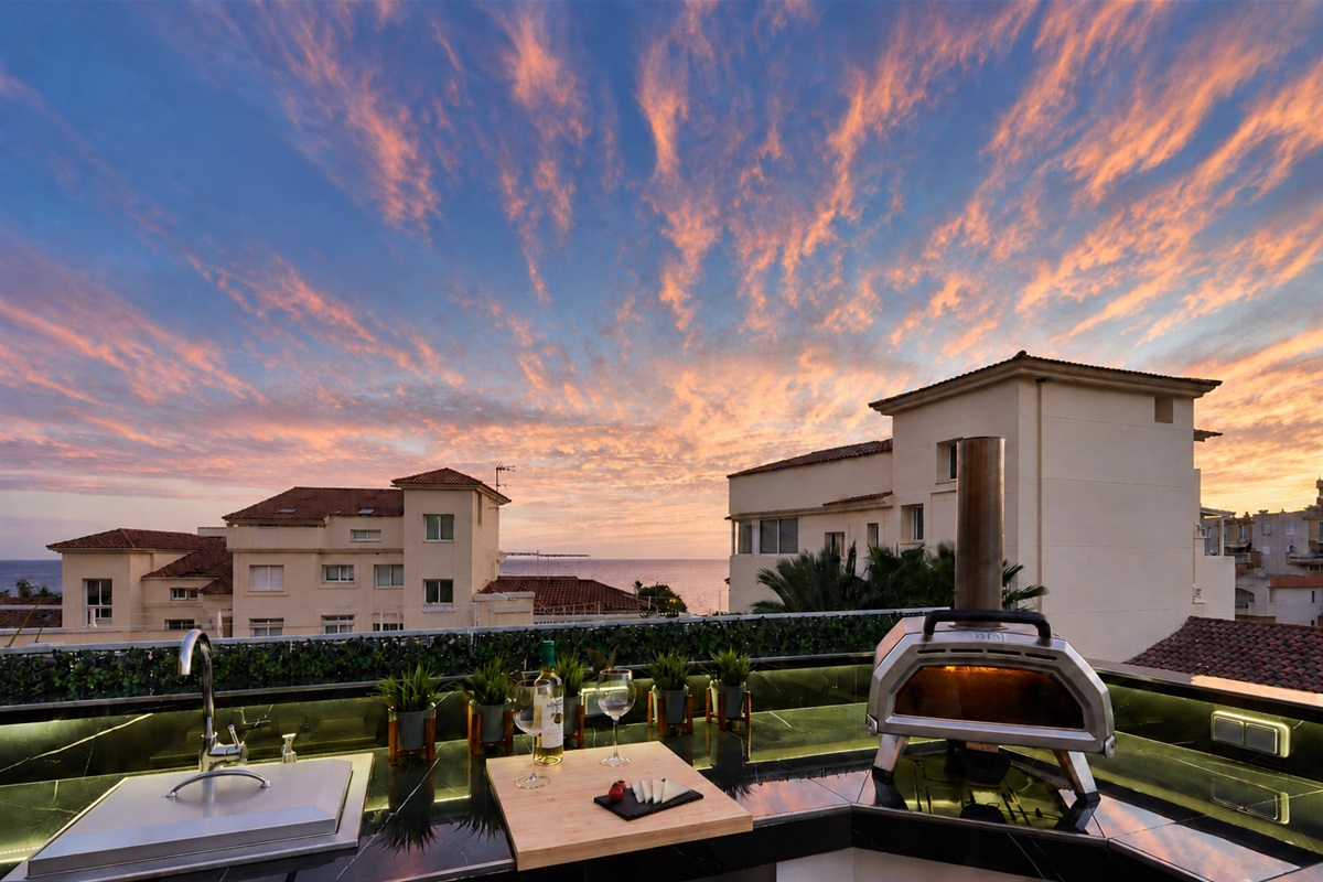 Fire up the built-in barbecue or the wood-fired pizza oven and enjoy cooking with a view. The fully equipped outdoor kitchen features a sink, fridge, and prep space with subtle lighting for evening meals. Dine under the open sky at the outdoor table, surro