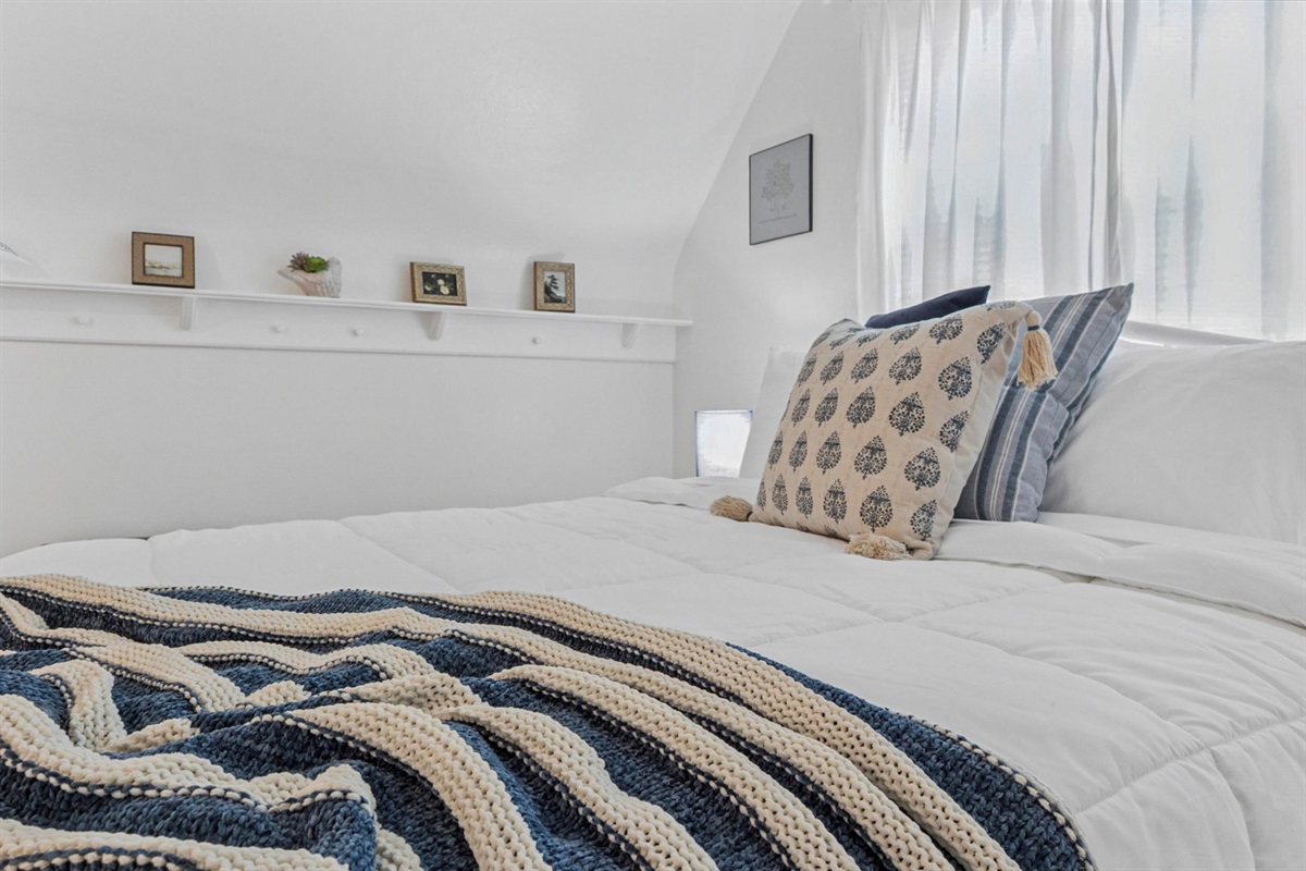 Soft textures and inviting layers—our upstairs queen bed at the South Bend guest retreat features a cozy throw and plush bedding, perfect for restful nights near Notre Dame.