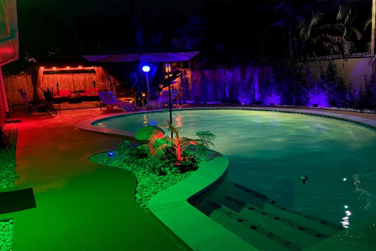 Nighttime view of Garden of Manors’ heated pool, featuring ambient LED lighting, tropical landscaping, and a serene island centerpiece designed for relaxed evening swims.