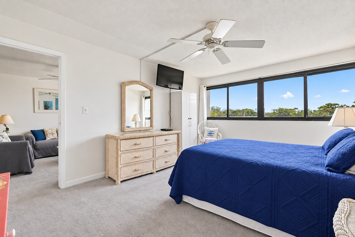 Queen bedroom with wide window views, wall-mounted TV, dresser storage, and direct access to the living room.