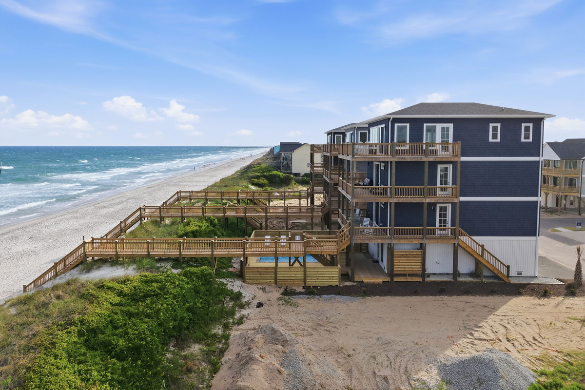 Aerial view highlighting the private pool deck and outdoor living space, connected to the home with multiple levels of decking and a direct boardwalk path leading toward the beach