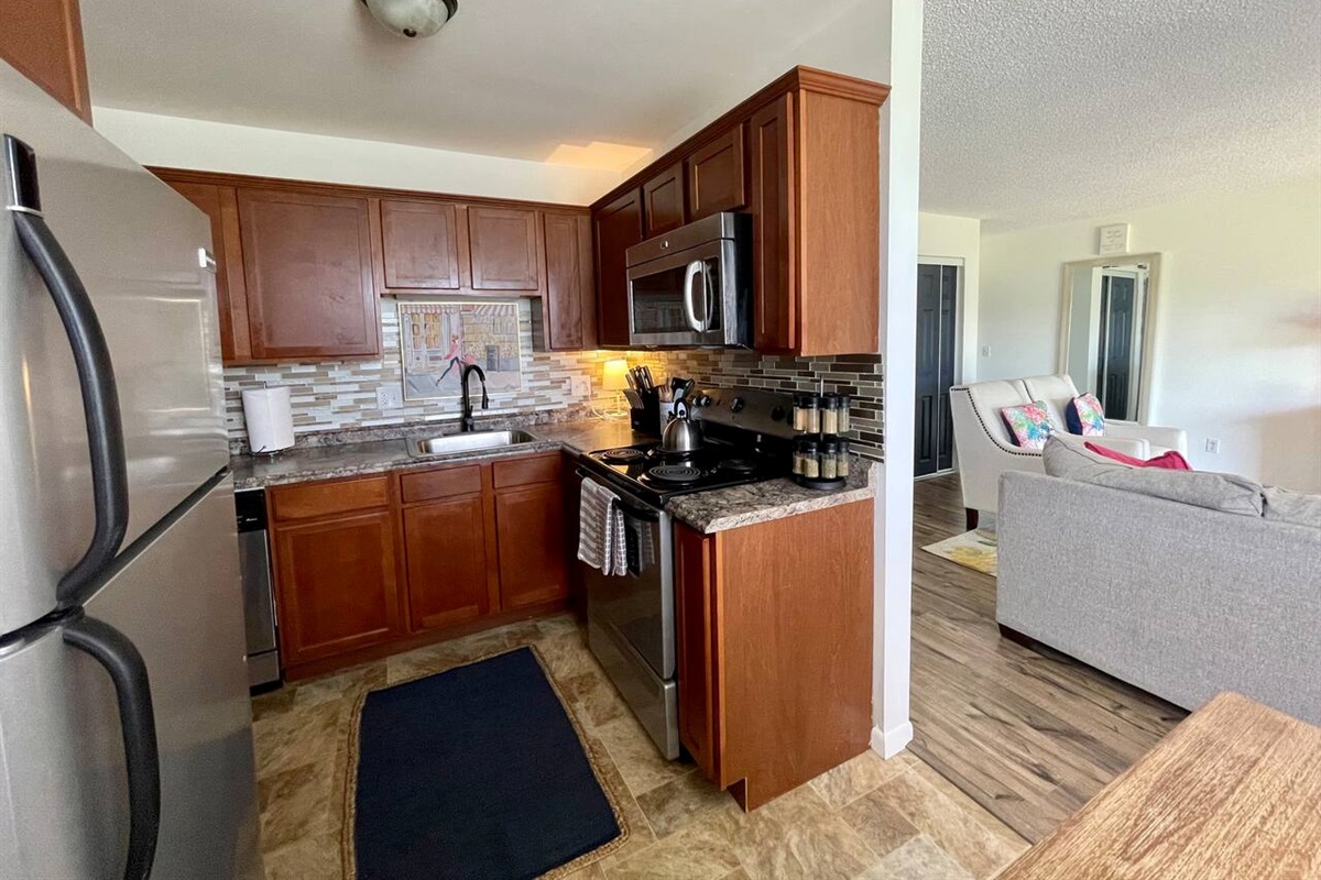 Charming kitchen with stainless steel appliances, rich wood cabinets, and modern tile backsplash. Fully stocked with cookware and utensils, this inviting space flows seamlessly into a cozy living area—perfect for relaxing or entertaining.