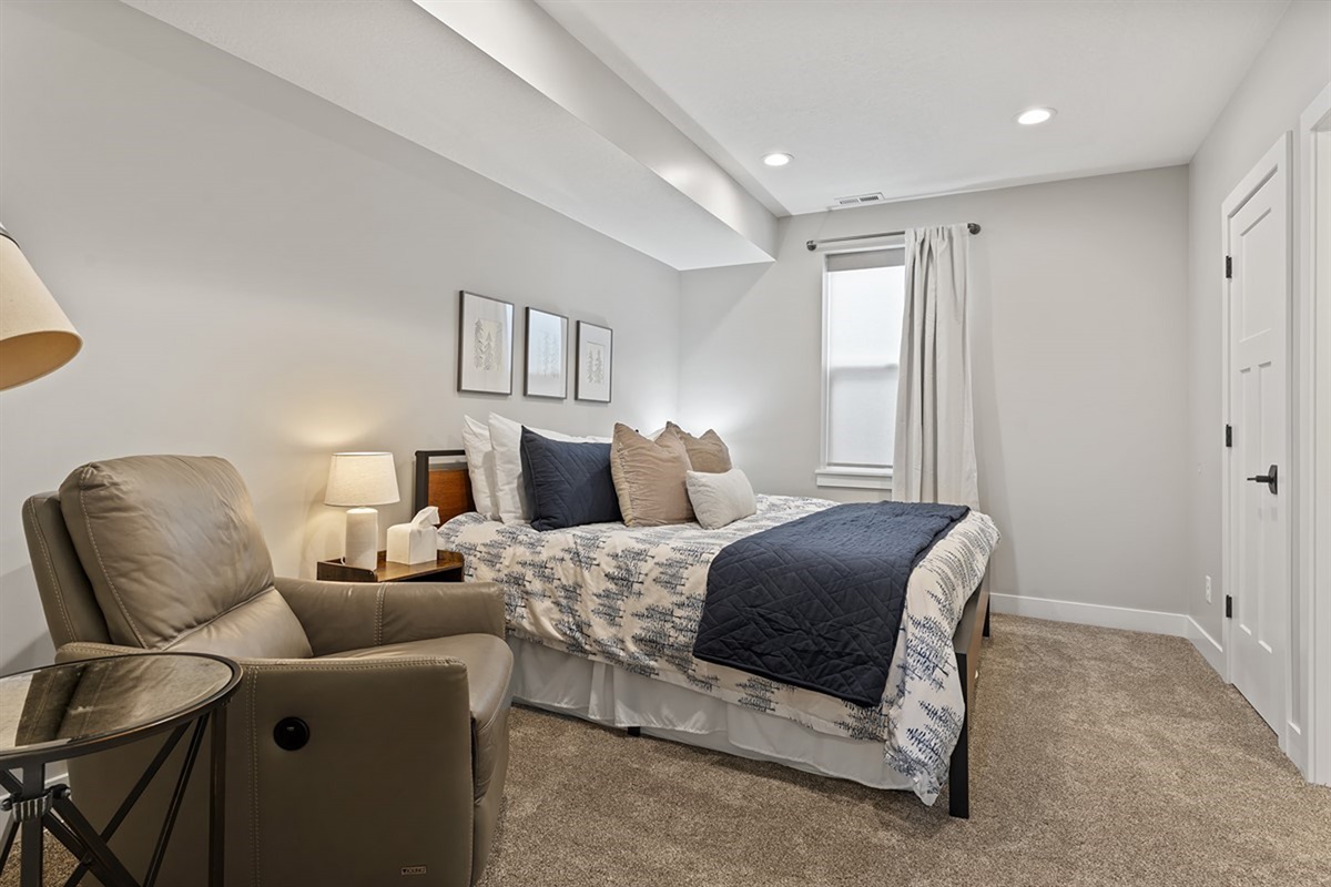 Cozy lower-level bedroom with plush bedding and a relaxing reading chair
