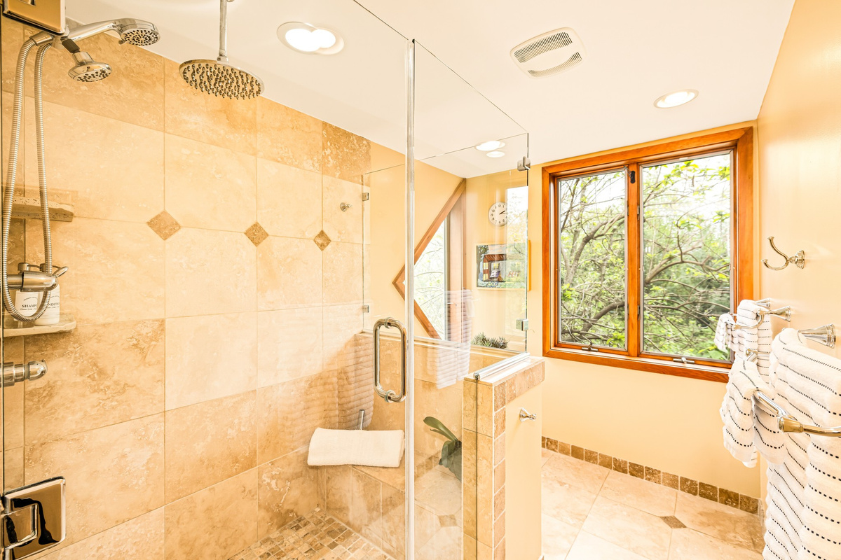 A true spa retreat: The primary bath with walk-in shower, dual rainfall heads, and a built-in bench. Enjoy the peaceful forest views for a calm start or end to your day.