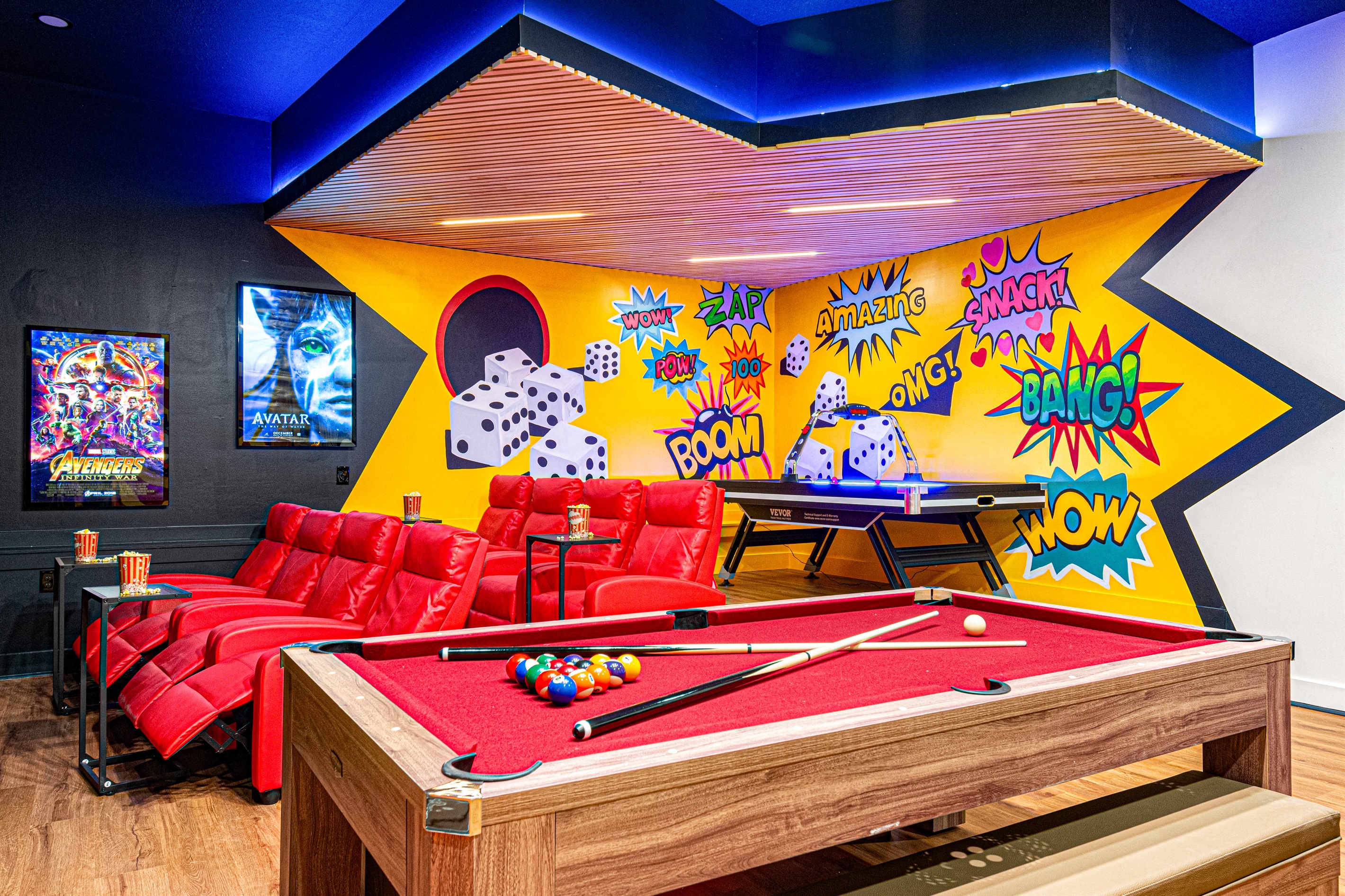 Step into the vibrant movie and game room featuring plush recliners, a pool table, air hockey, and a dynamic comic-style mural. The ultimate spot for entertainment and fun-filled nights!