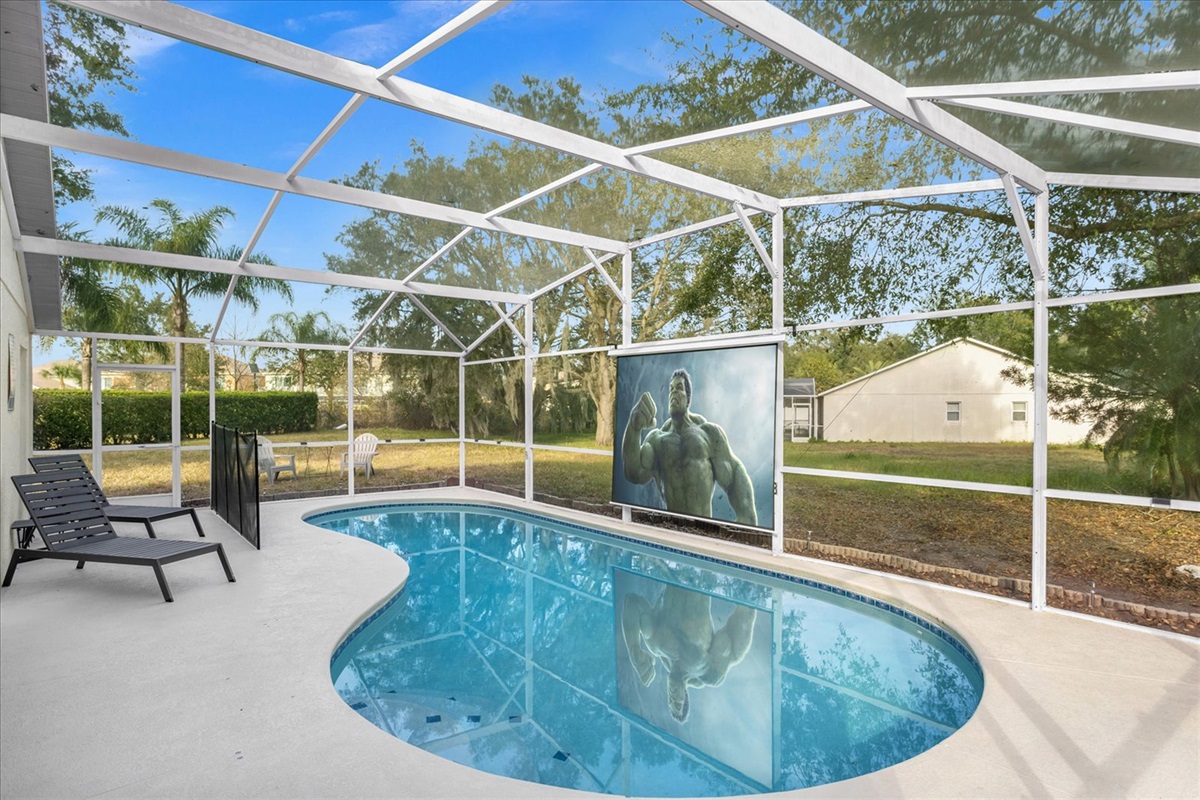 Private screened pool area with outdoor seating and a large movie screen for entertainment.