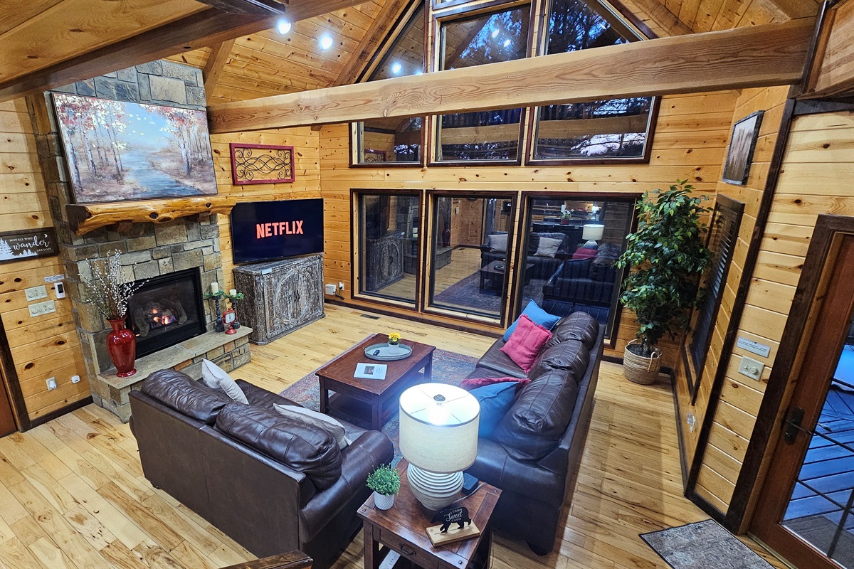 Warm, open great room with leather sofas, a crackling fireplace, and a towering window wall to the trees.