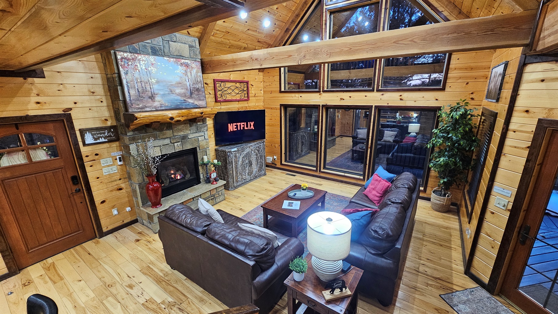 Warm, open great room with leather sofas, a crackling fireplace, and a towering window wall to the trees.