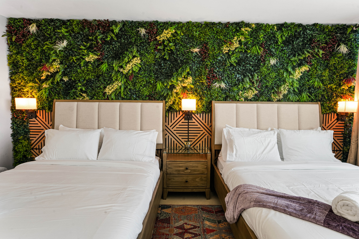 Both queen beds sit side by side under the signature greenery and wood-panelled wall, each with a dimmable wall sconce and USB charging.