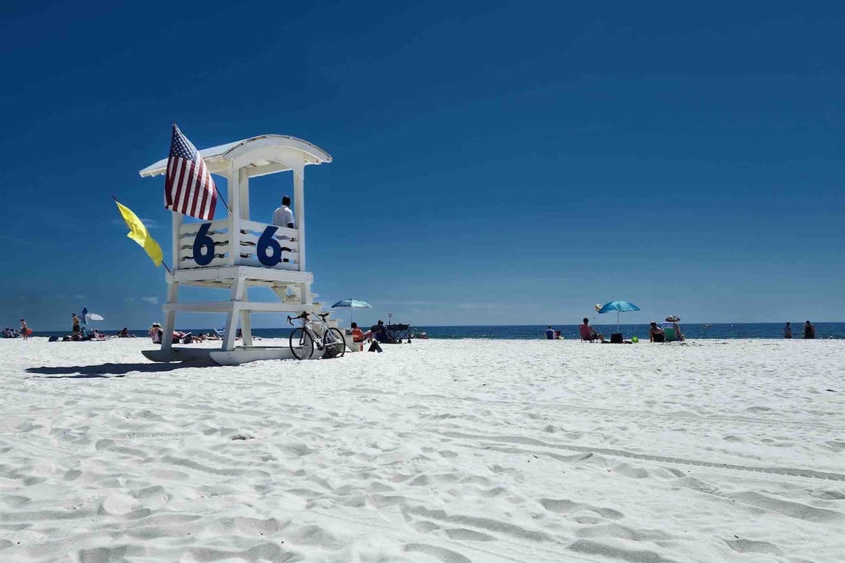 Enjoy a serene view of the private, white-sand beach with a lifeguard tower and ocean waves, ensuring a safe and relaxing experience.