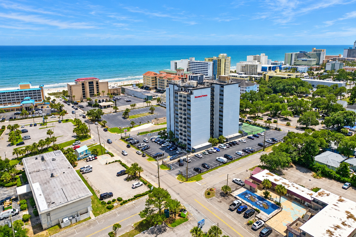 Aerial view of Holiday Towers with shared pool, hot tub, sports court, parking, and Myrtle Beach attractions nearby.