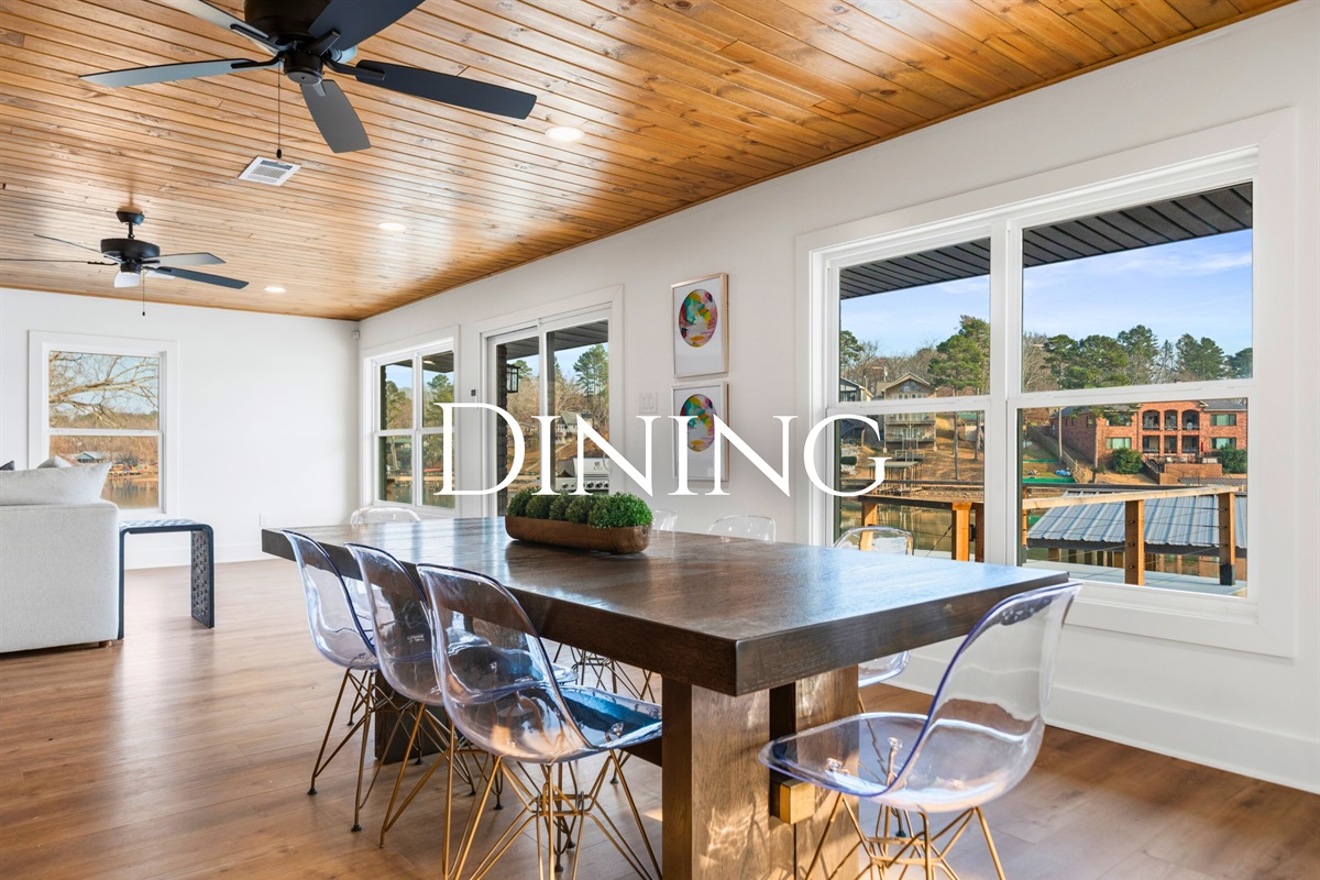 A large dining table sits beside wide windows, offering a wonderful spot to enjoy meals together while taking in views of the lake.