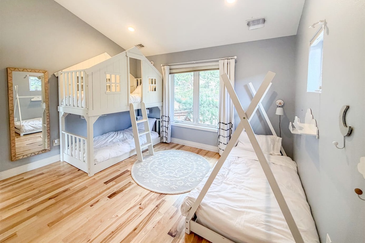 This bright bedroom combines fun and comfort, featuring a playful bunk bed, a cozy teepee-style bed, and a soft rug for reading, playing, or relaxing