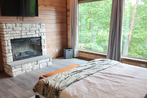 Bedroom with stone fireplace and large Nature-facing windows