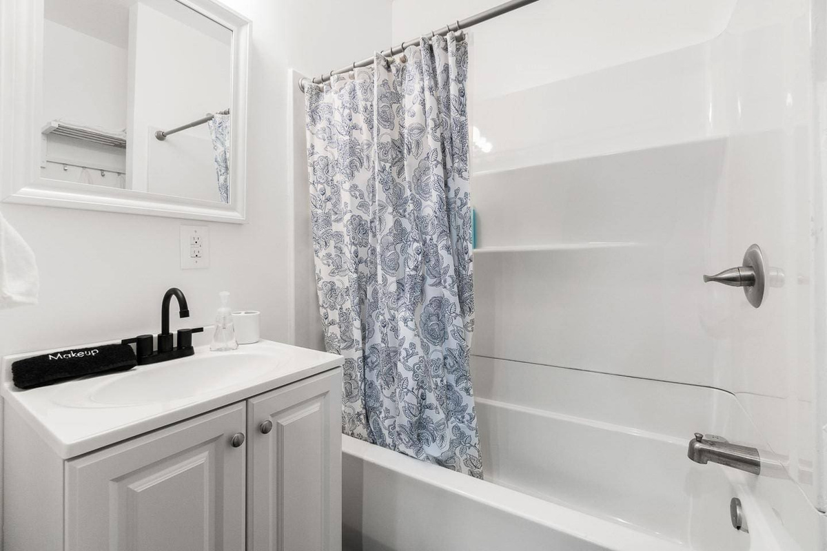 Bright and clean bathroom featuring a relaxing tub, mirror, fresh towels, and essentials like soap, shampoo, and conditioner for your convenience.