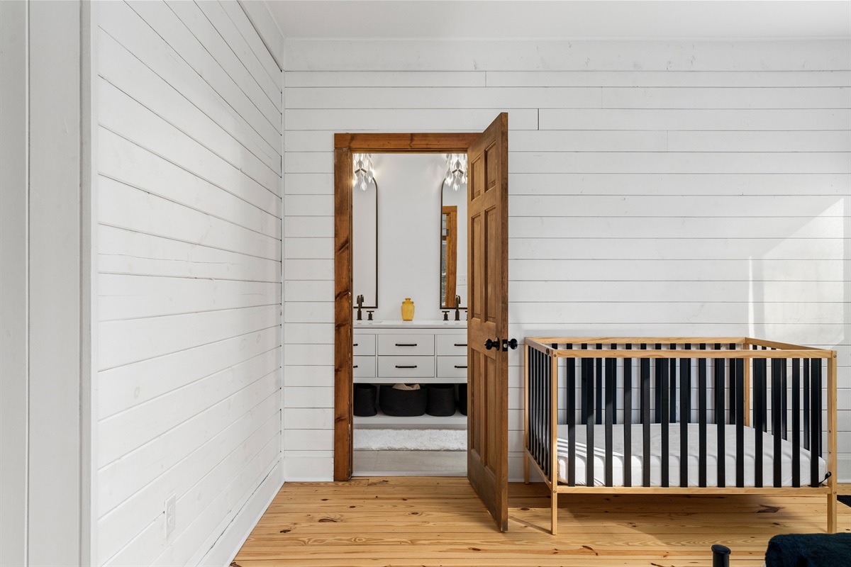Bedroom 2: Bright room with a sleek crib, inviting natural light, and a charming wood door.