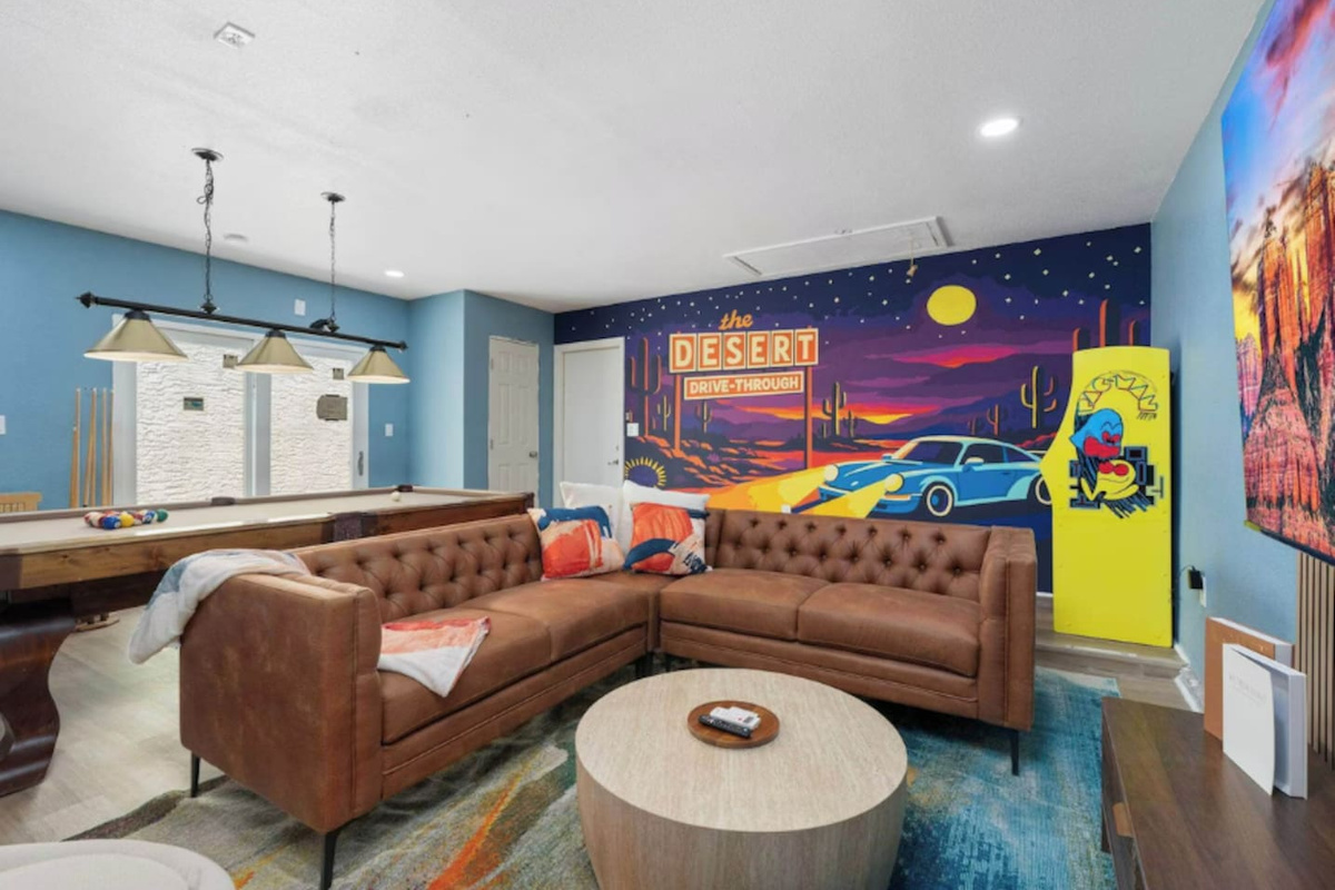 Playroom with vintage desert mural, leather seating, pool table, and arcade games—a fun, colorful space for all ages.