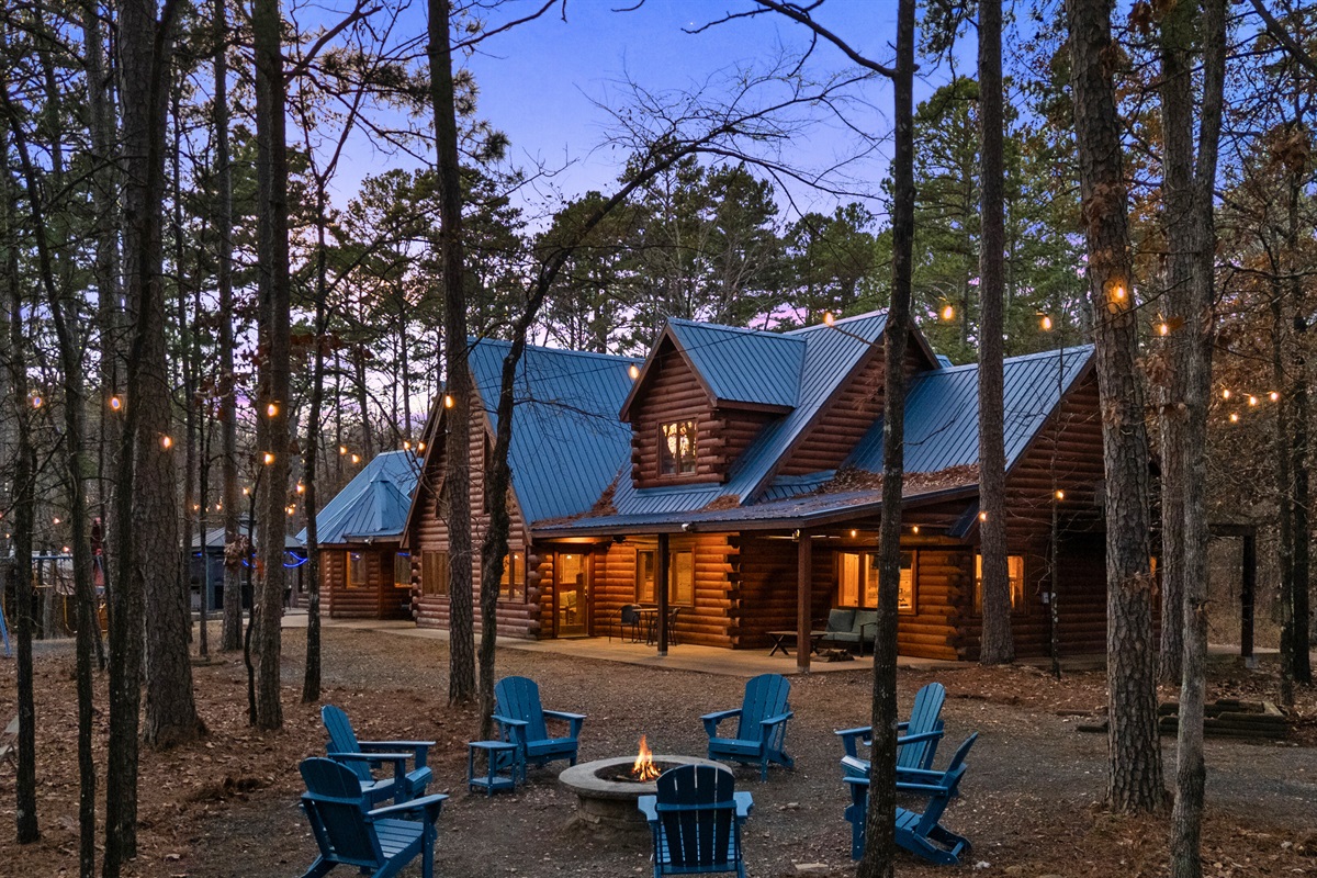 As dusk settles in, the cabin lights create a warm and welcoming glow against the wooded backdrop.