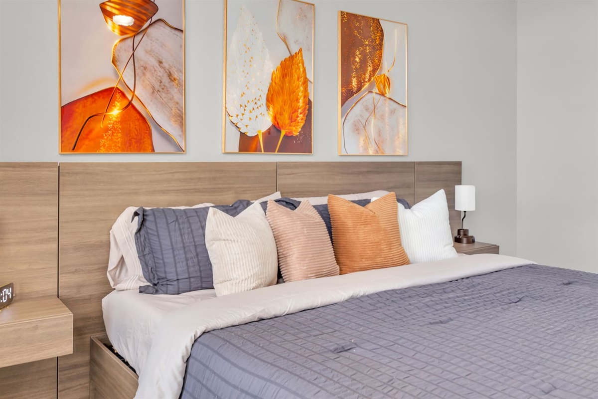Spacious primary suite featuring a king bed, comfortable sitting area, room-darkening shades, ceiling fan, modern artwork, fresh bed linens, hangers, and Smart TV access for a relaxing retreat.