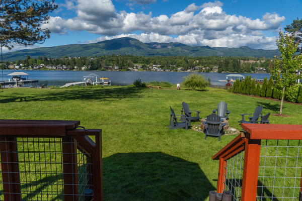 An expansive grassy backyard leads to the lake, where a dock and fire pit invite evenings outdoors. The open lawn is perfect for relaxing or playing, while the shoreline and gentle water create a peaceful connection between land and lake.