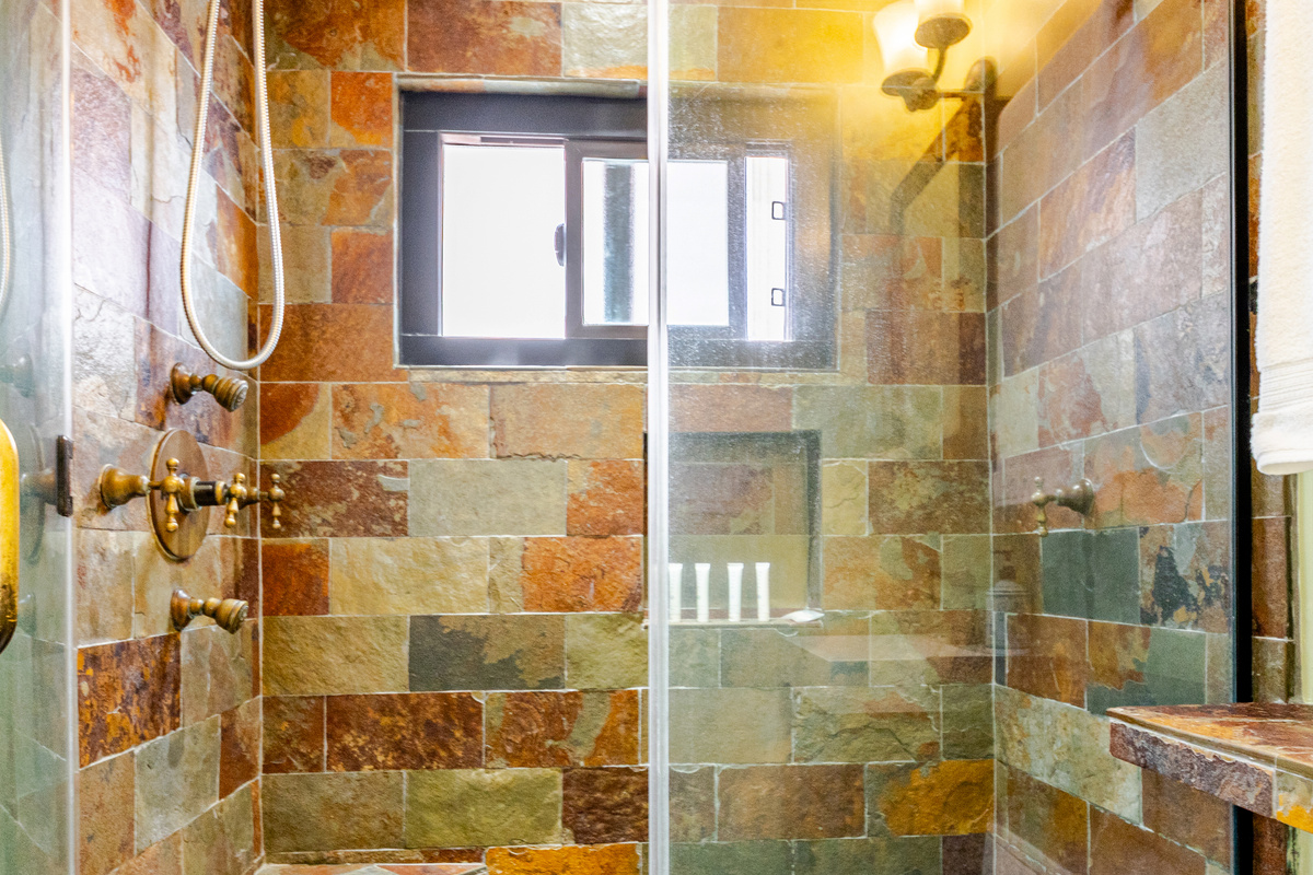 Bathroom stand-up shower includes slate tile, 2 rain shower heads, 2 body jets, river rocks and a glass shower door.