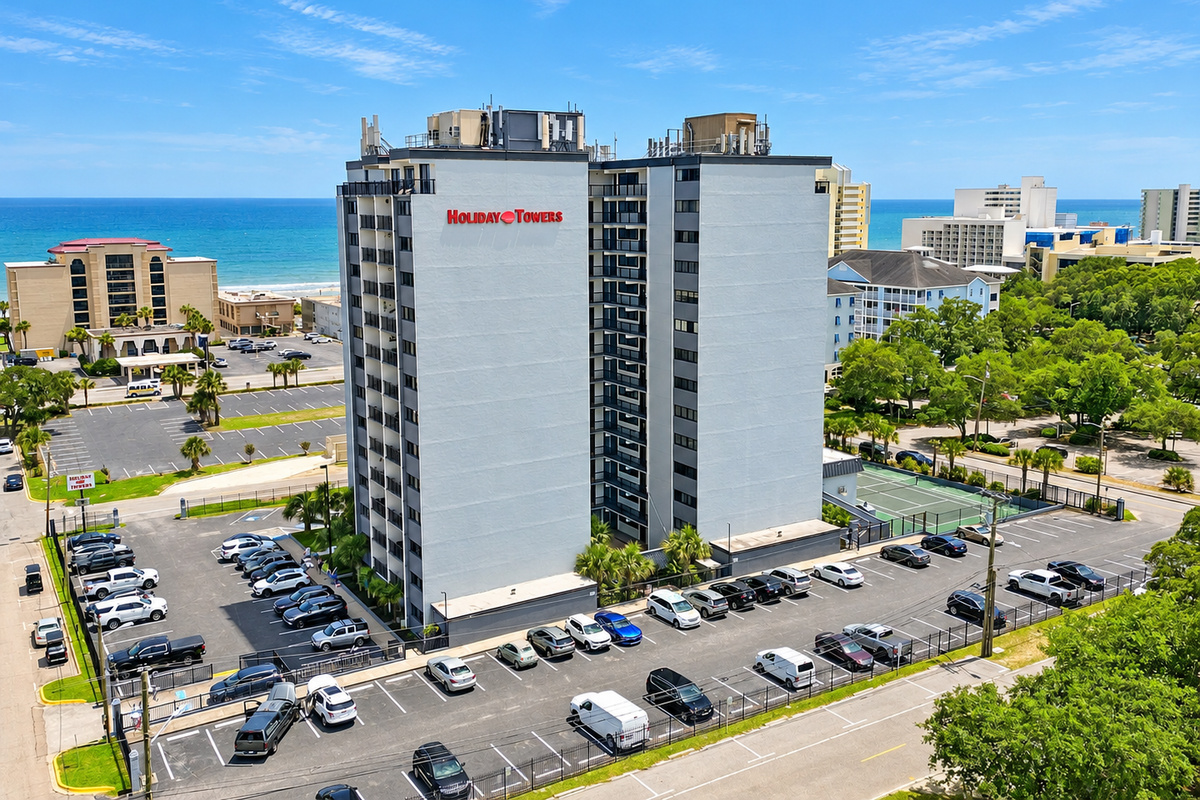 Aerial view of Holiday Towers with shared pool, hot tub, sports court, parking, and Myrtle Beach attractions nearby.