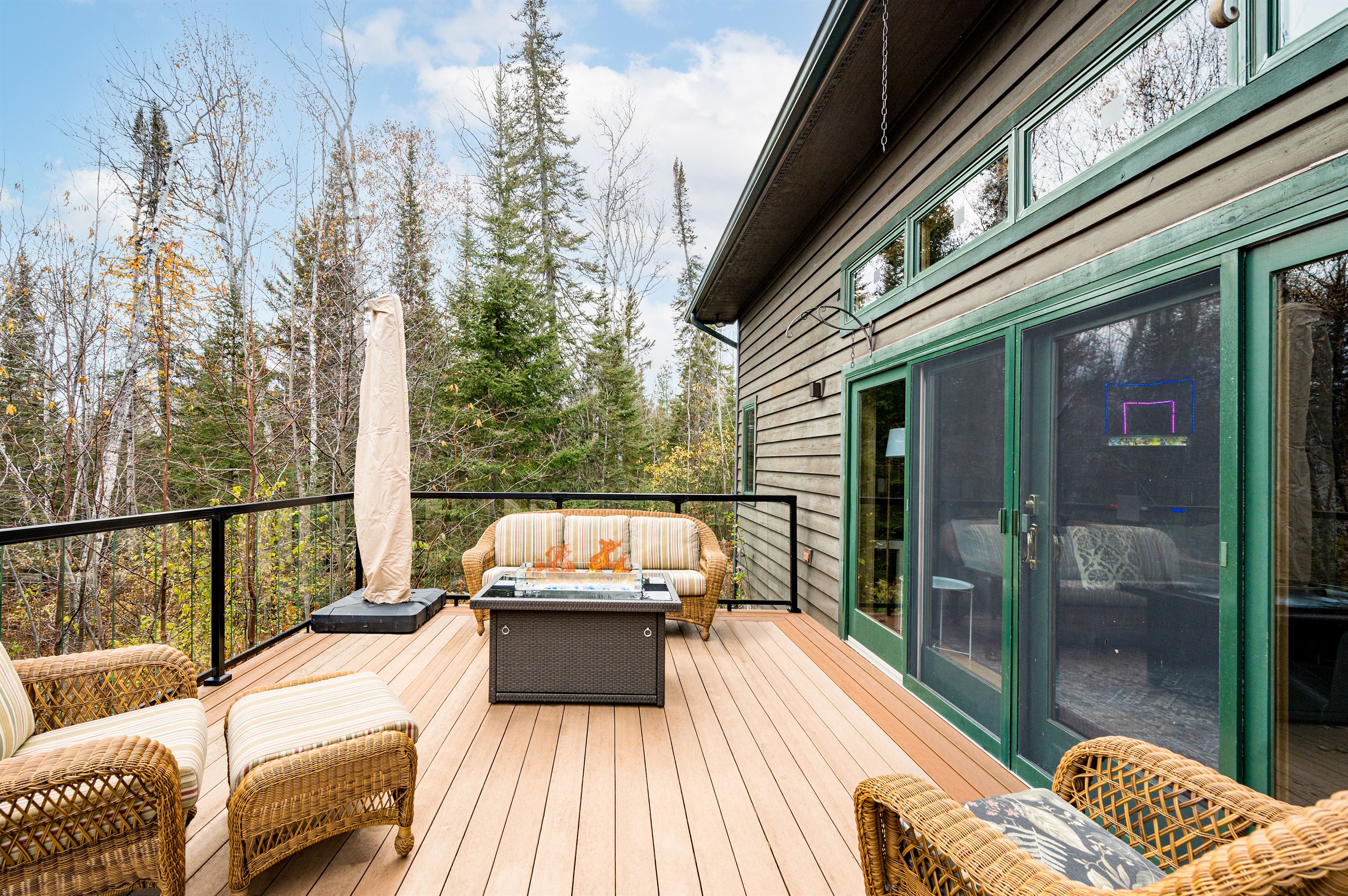 A serene outdoor patio surrounded by forest views, featuring cozy wicker seating and a fire table perfect for morning coffee, evening chats, or stargazing in peaceful comfort.