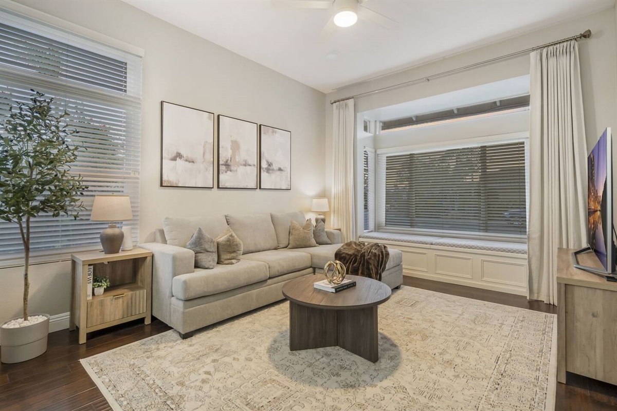 A cozy living room features a pull-out queen sofa bed, perfect for guests, and a 65" Smart TV for entertainment. It has a charming window seating area and side tables equipped with charging stations, offering convenience and comfort for everyone