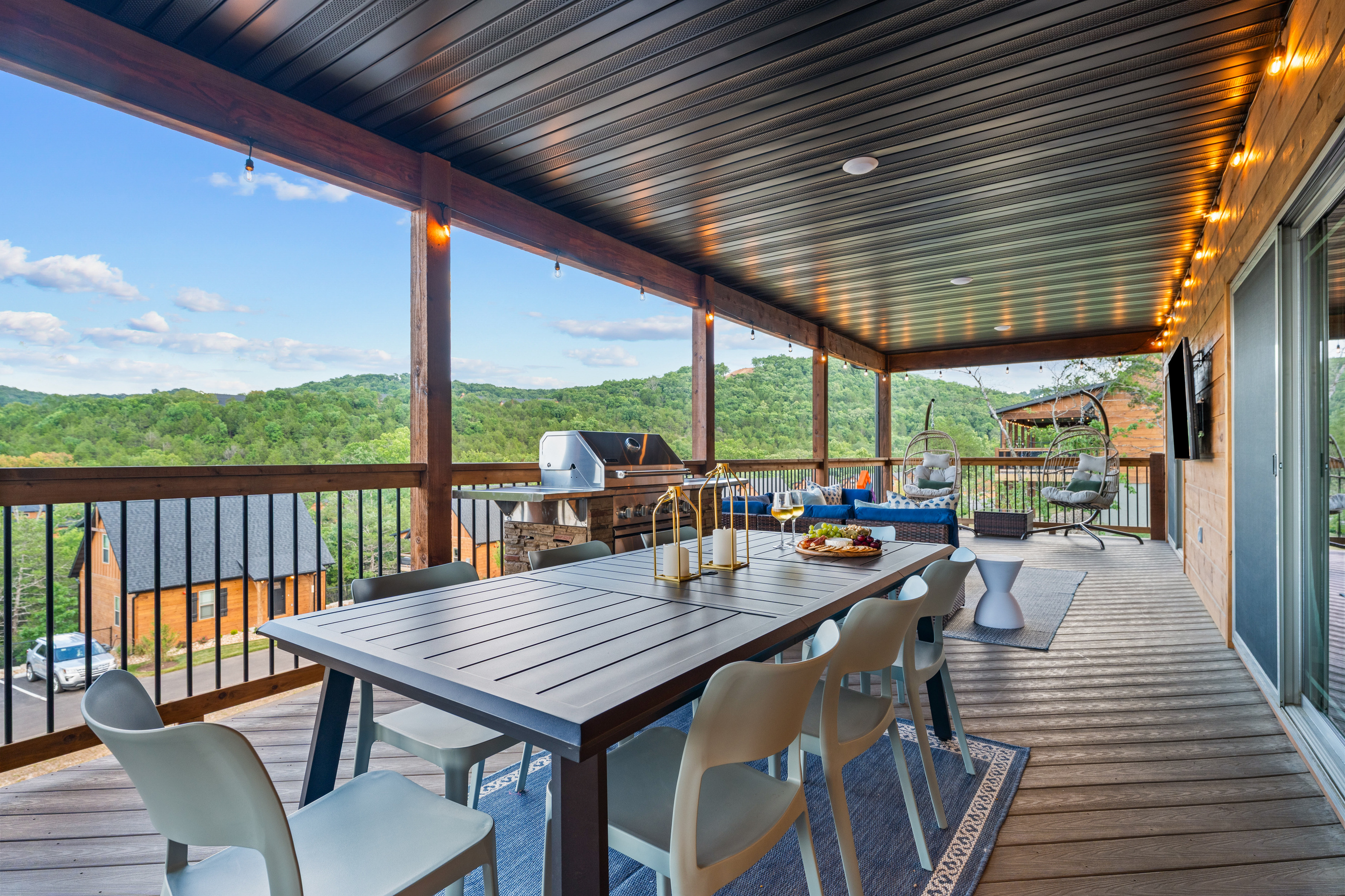 The expansive covered deck offers group dining, a gas grill, a fire-table lounge, and panoramic Ozark hill views.
