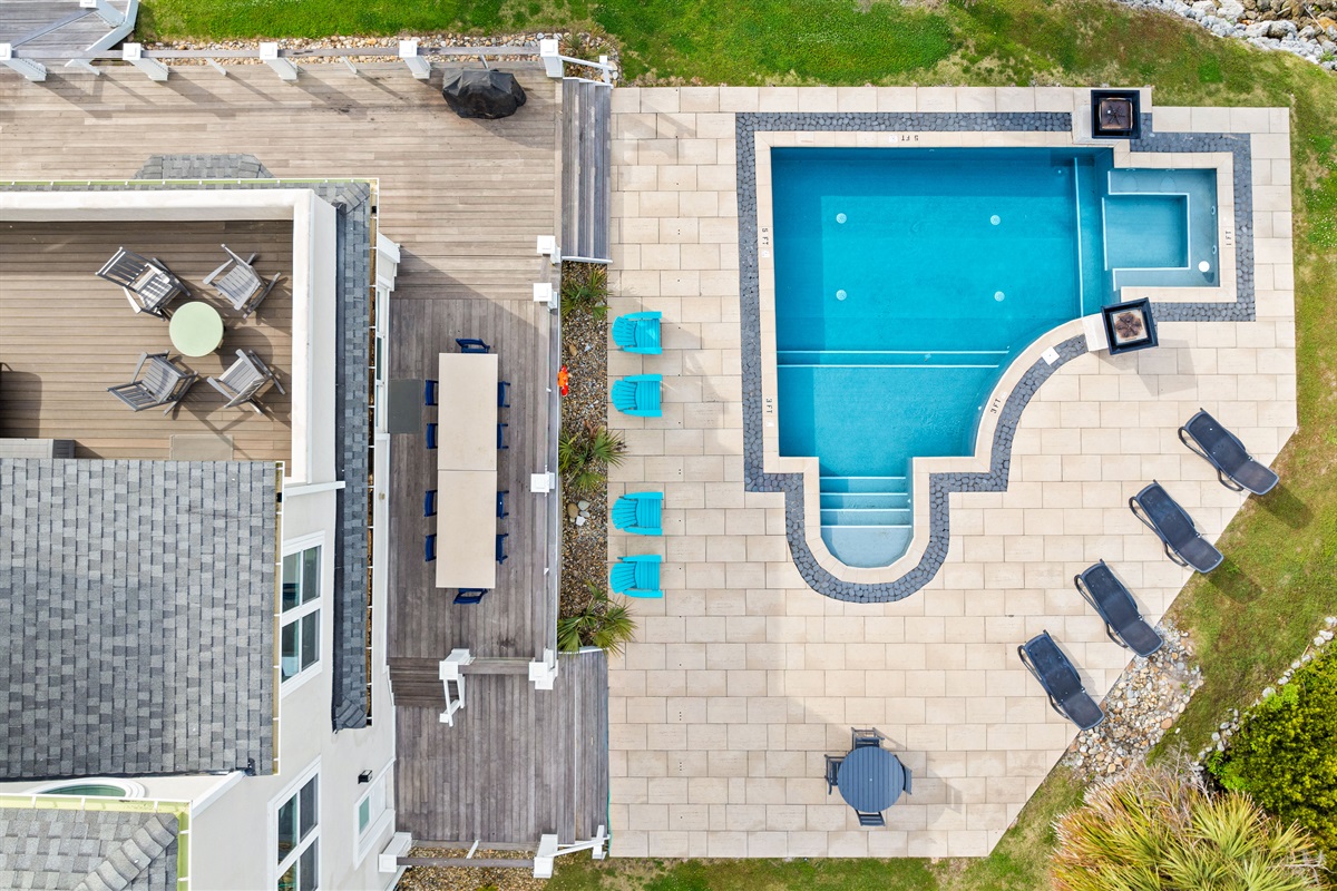Aerial view showcasing the spacious pool deck, outdoor dining, and waterfront layout