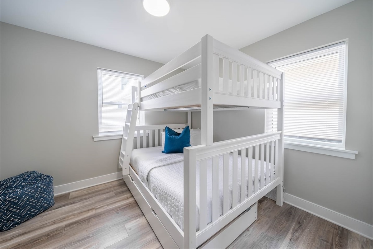 Bright bunk bedroom with sturdy twin bunk beds, fresh white linens, and natural light from dual windows. Designed for comfort and practicality, it offers a relaxed sleeping setup ideal for kids or additional guests.