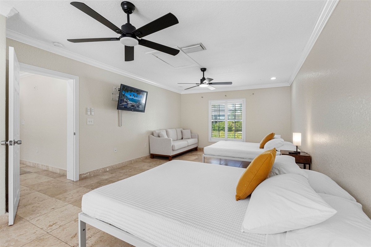This bright and airy bedroom features two comfortable beds, a cozy sitting area, and a wall-mounted TV for ultimate relaxation.