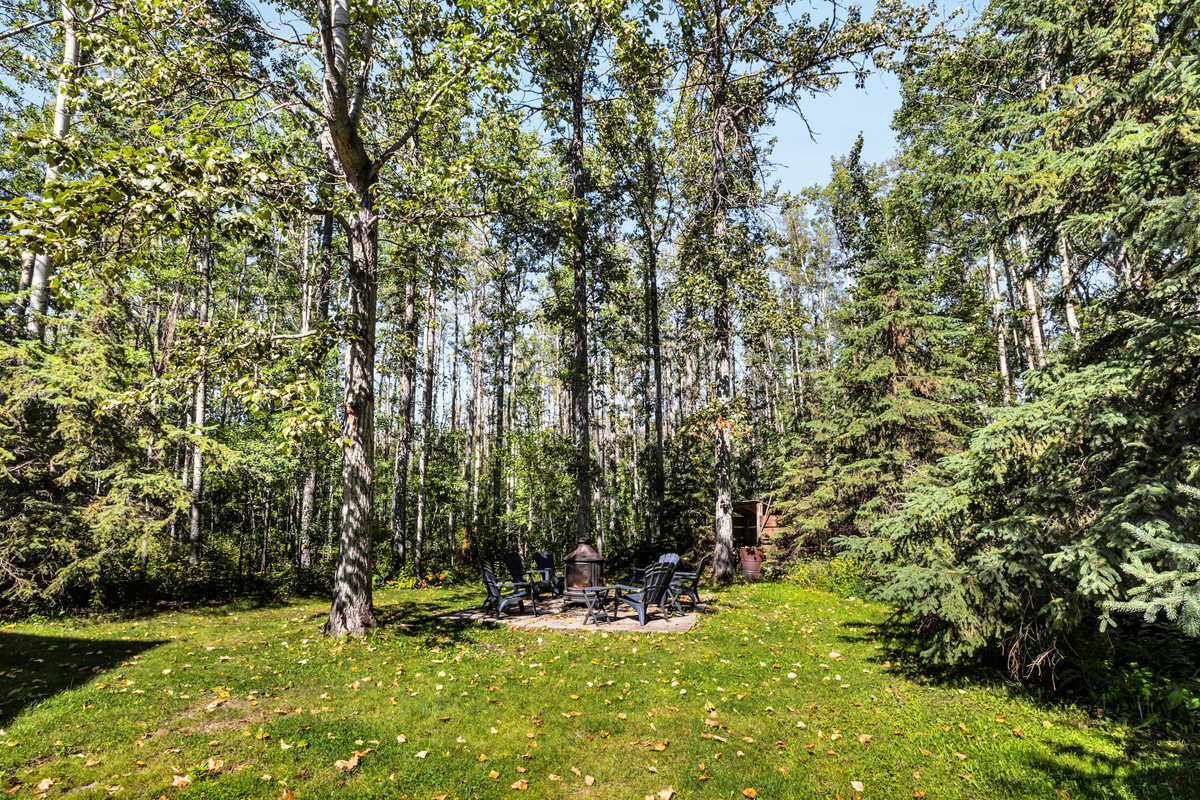 A generous lawn and mature trees create a peaceful backyard setting, with the firepit tucked away for cozy evenings outdoors.