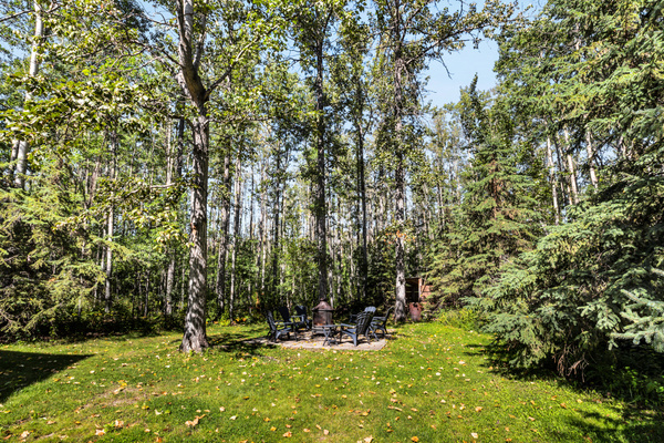 A generous lawn and mature trees create a peaceful backyard setting, with the firepit tucked away for cozy evenings outdoors.