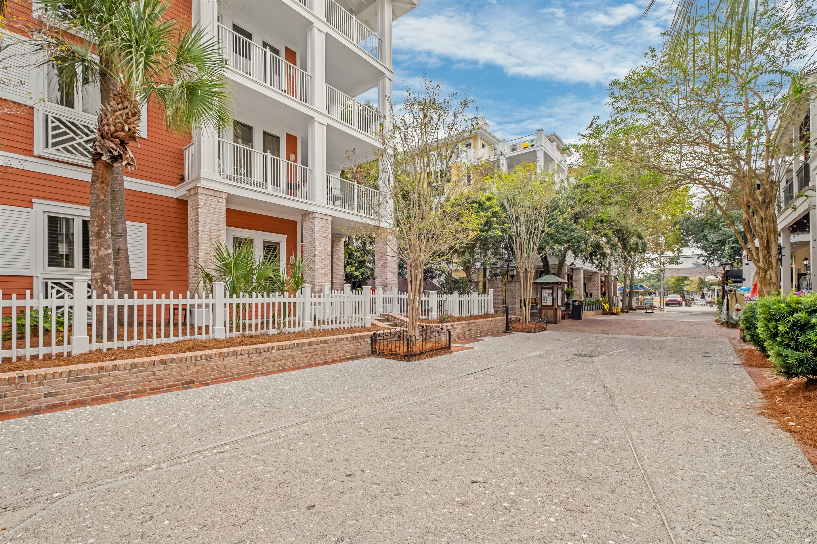A quiet, picturesque street view leading to the entrance of the elegant townhome, surrounded by lush trees and stylish fencing for added privacy.
