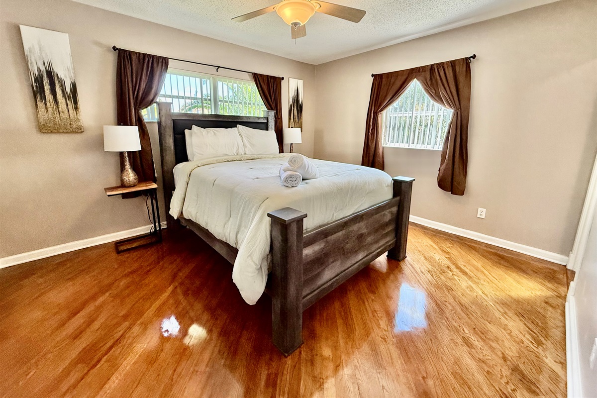 Unwind in this serene space, complete with soft bedding, blackout curtains, and natural light streaming in from multiple windows.