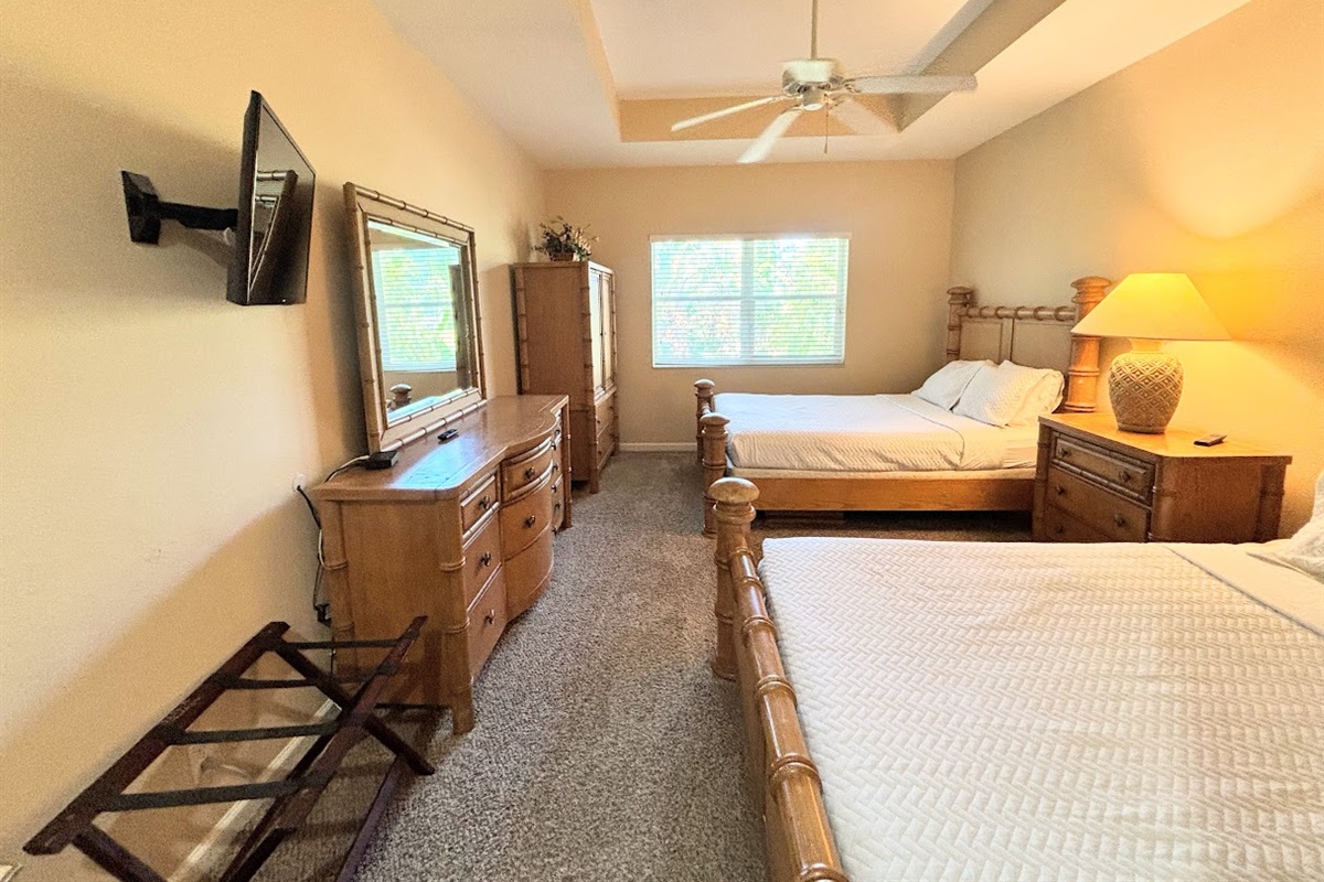 Spacious bedroom featuring two comfortable beds, tray ceiling with ceiling fan, cozy seating area, and plenty of natural light.