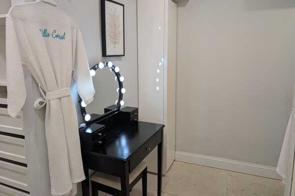Dedicated black makeup vanity table with a lighted Hollywood mirror, matching chair, and a plush embroidered Villa Coral robe in the primary suite at Villa Coral in Dorado, Puerto Rico.
