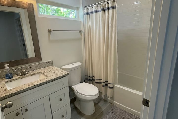 A real tub means bubble baths after sandy adventures — this full bath pairs a granite vanity with a shower/tub combo and soft light from the transom window. Rubber ducks and bath crayons are welcome travelers here.