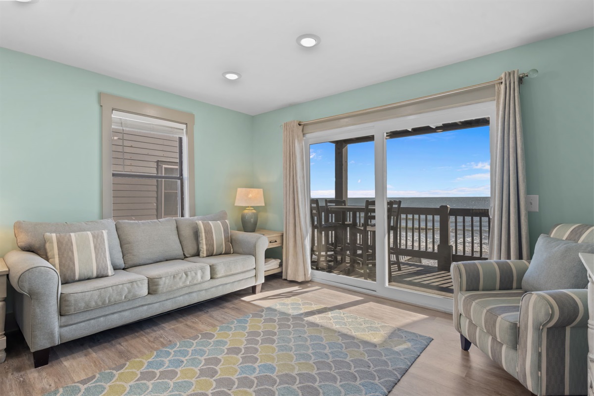 Bright and breezy living space featuring comfortable seating, coastal d&eacute;cor, and sliding glass doors that open to a private oceanfront balcony
