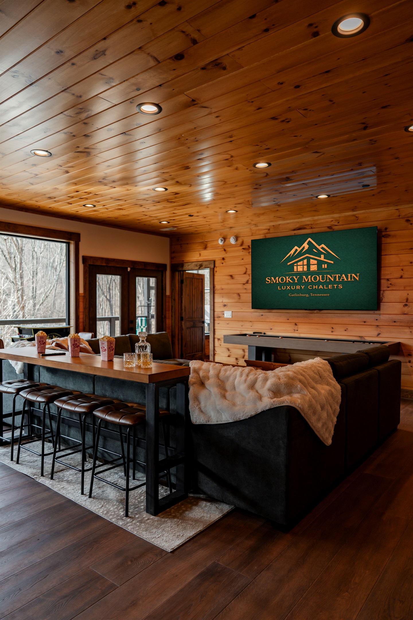 Perfect for game day, movie nights, or family fun, featuring a 100” TV, cozy sectional seating, and bar stools so everyone has a great view.