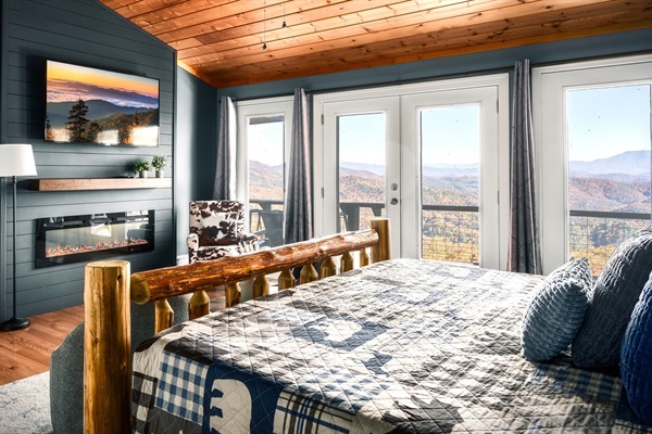 Enjoy that beautiful view right from your bed when you wake up! This is the Master Bed on the main floor complete with electric fireplace combined with floor to ceiling glass door and window overlooking the AMAZING mountain view.