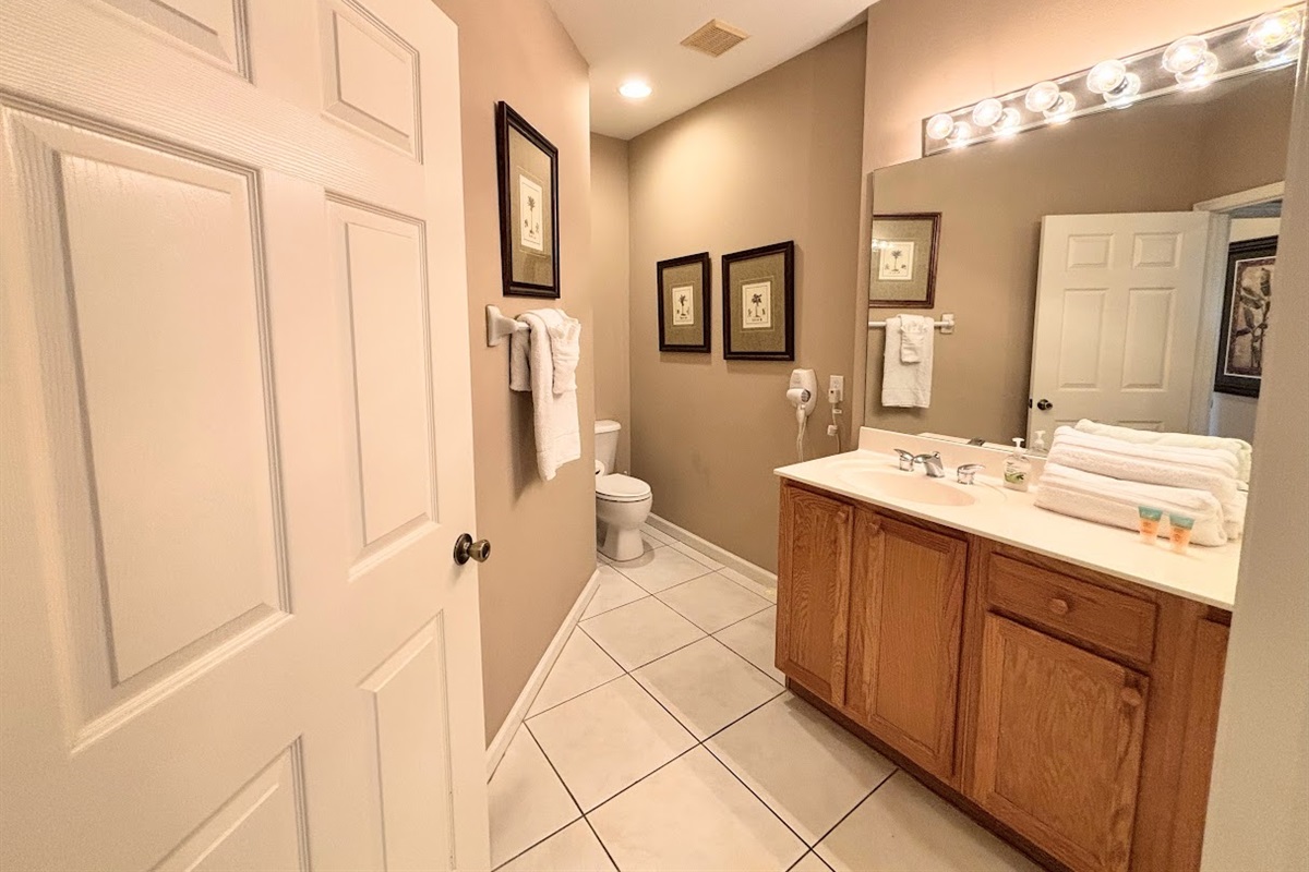 Clean and spacious bathroom featuring a large vanity, bright mirror lighting, tile flooring, and plenty of counter space.