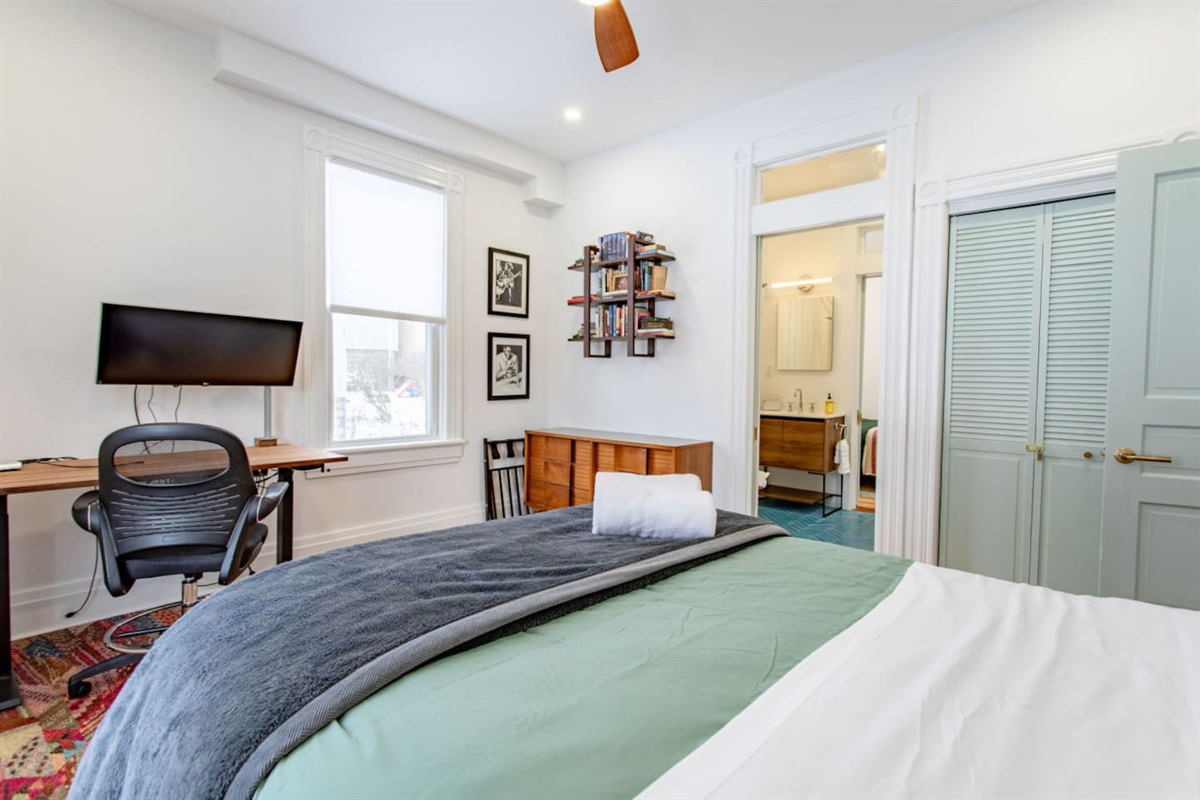A bedroom featuring a cozy bed, a dedicated workspace with a desk and chair, and an adjacent bathroom, offering a functional and comfortable space for both relaxation and productivity.