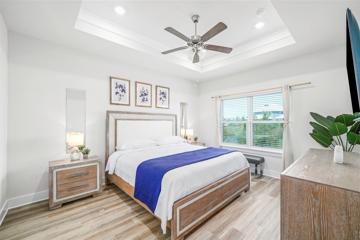 Primary Suite: Modern king bedroom featuring an en suite bathroom, plush linens, ceiling fan, elegant bedside lamps, dresser, and Smart TV.