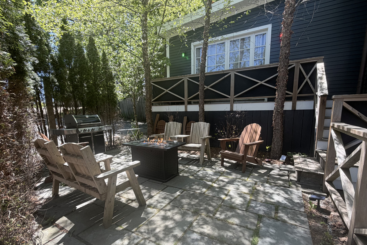 The stone patio features a gas fire table, folding composite Adirondacks, a BBQ grill, and solar string lights. The balcony above displays green and red port and starboard navigation lighting, extending the ship-inspired theme to the outdoors.
