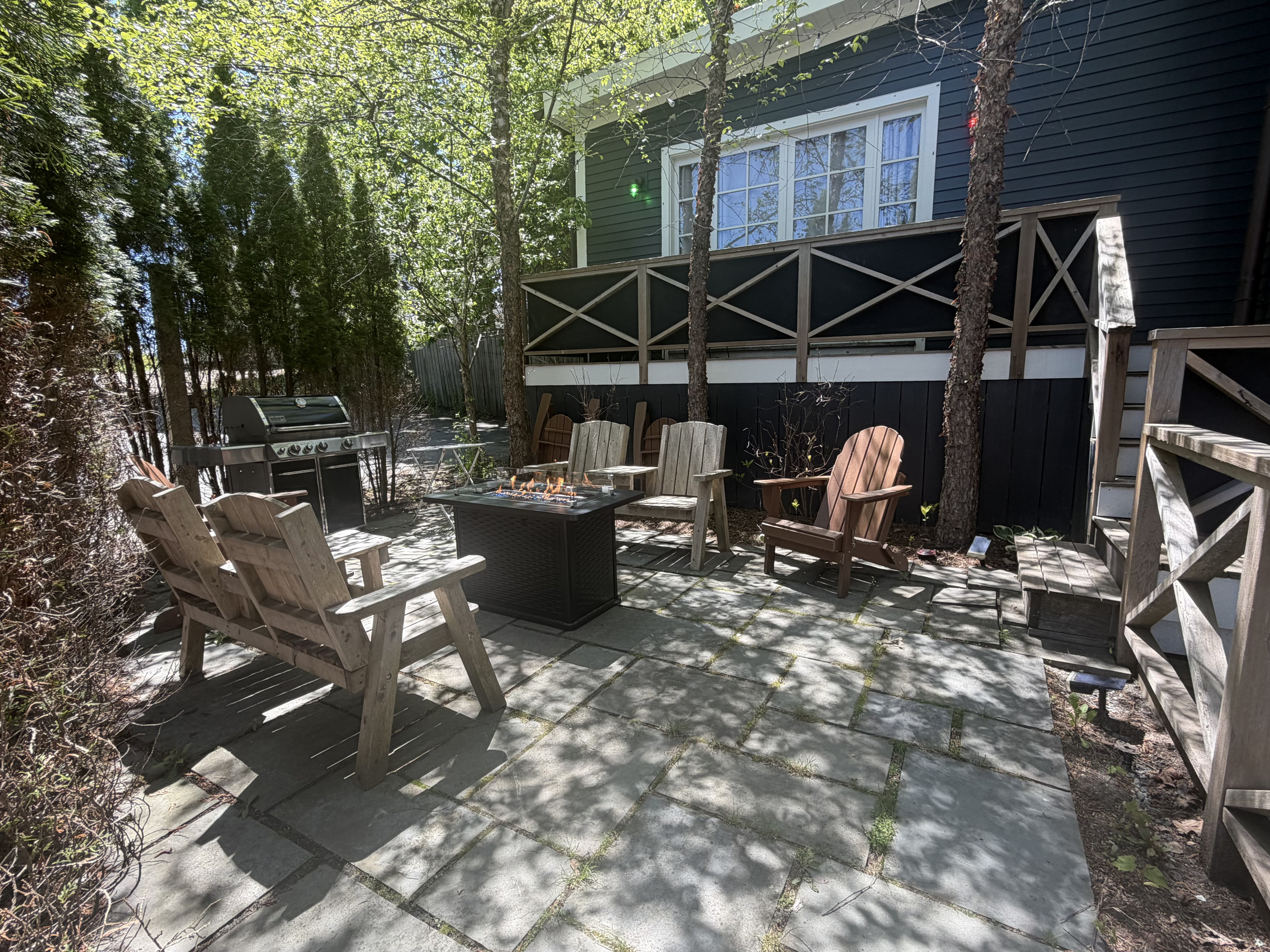The stone patio features a gas fire table, folding composite Adirondacks, a BBQ grill, and solar string lights. The balcony above displays green and red port and starboard navigation lighting, extending the ship-inspired theme to the outdoors.