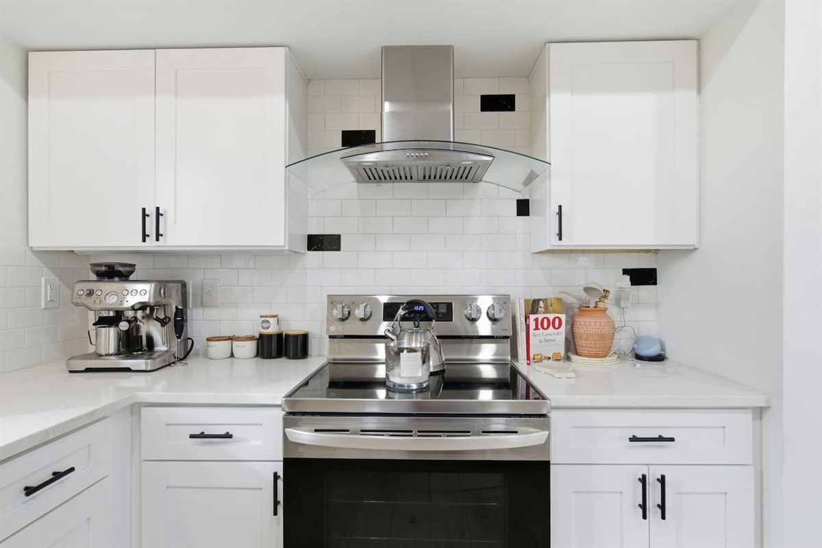 Stylish cooking space with stainless steel oven, range hood, microwave, tile backsplash, and modern cabinetry.