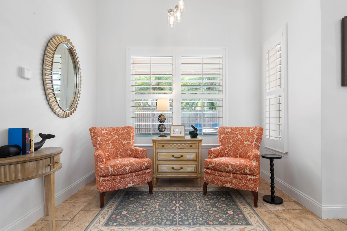 Quiet sitting nook with two coral armchairs by a shuttered window, a calm place to read while the house buzzes.
