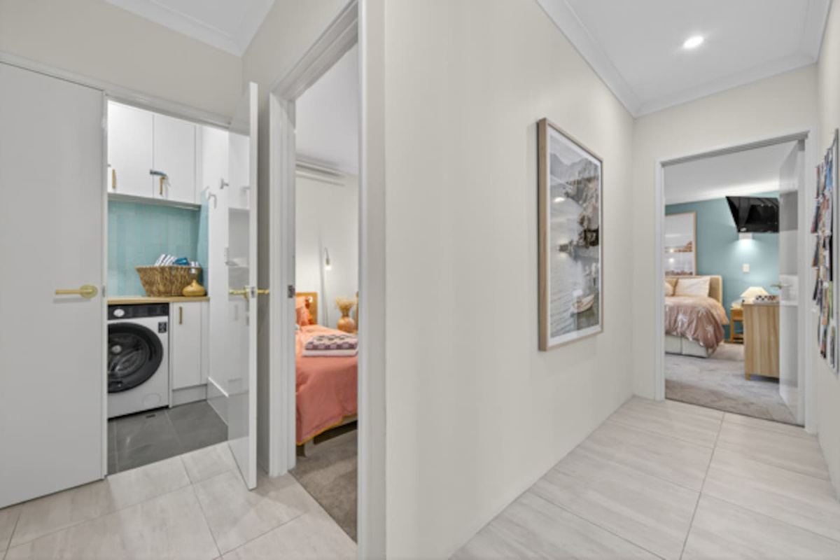 Bright tiled hallway connecting the laundry, the twin bedroom and the main bedroom with its wall-mounted TV, keeping the sleeping areas tucked away together.
